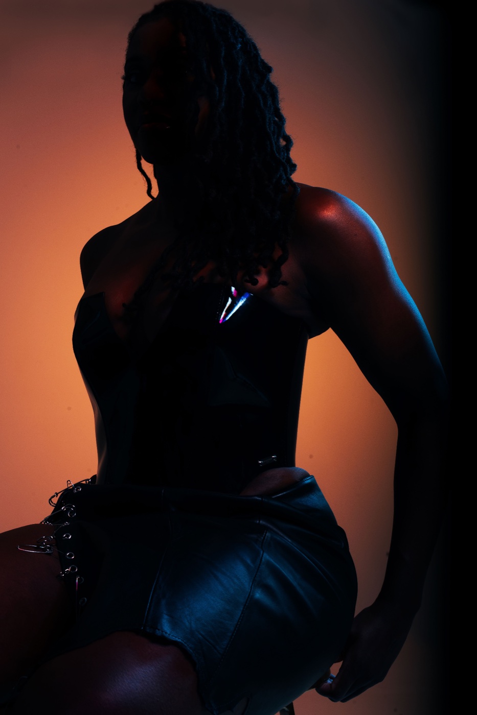 Domina Divinia in silhouette, rim-lit against a dark background.