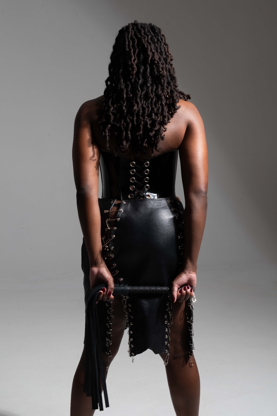 Domina Divinia, back view, in a black leather corset.